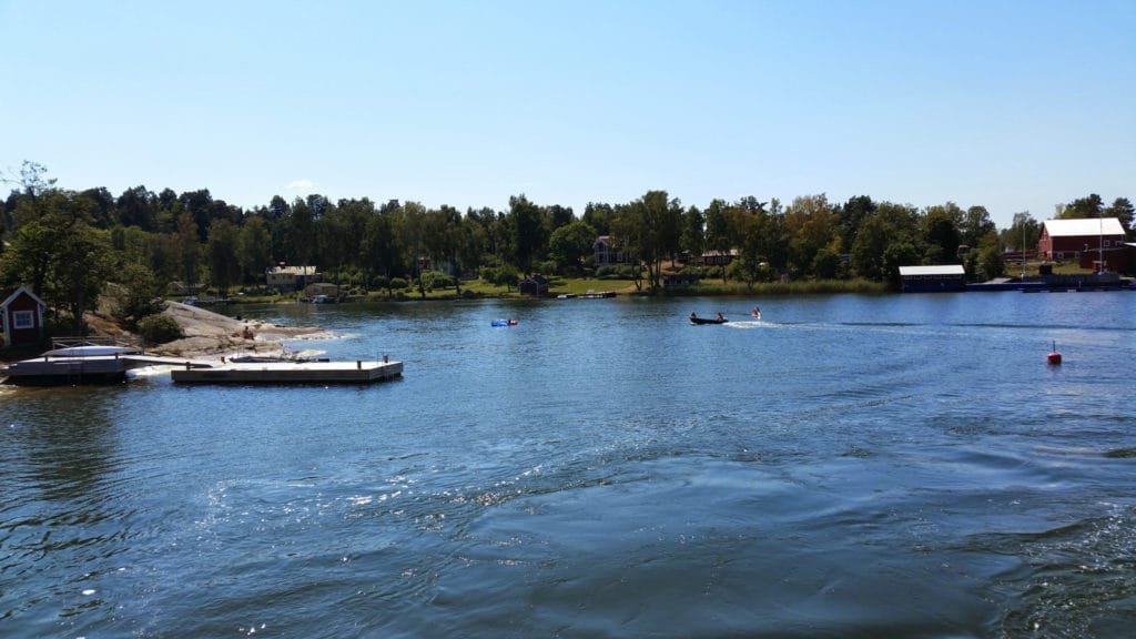 Utsikt over Stockholms skjærgård med brygger, skogkledd kystlinje og klar blå himmel.