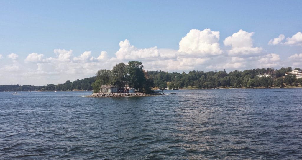 Liten øy med trær omgitt av rolig vann under en delvis skyet himmel i Stockholms skjærgård.