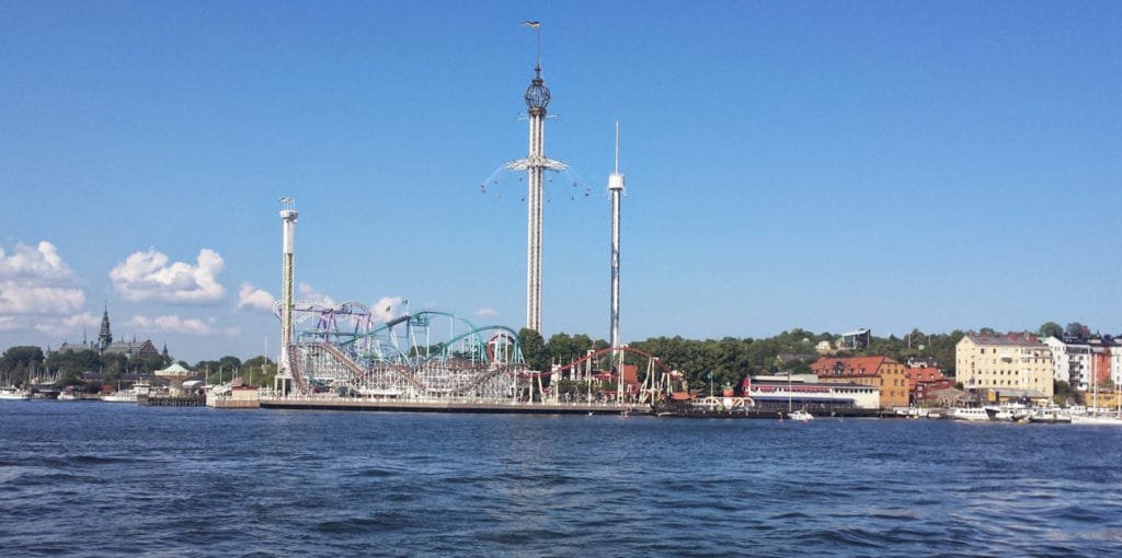 Bildet viser en fornøyelsespark ved vannkanten i Stockholms skjærgård med karuseller og andre attraksjoner under en klar blå himmel.