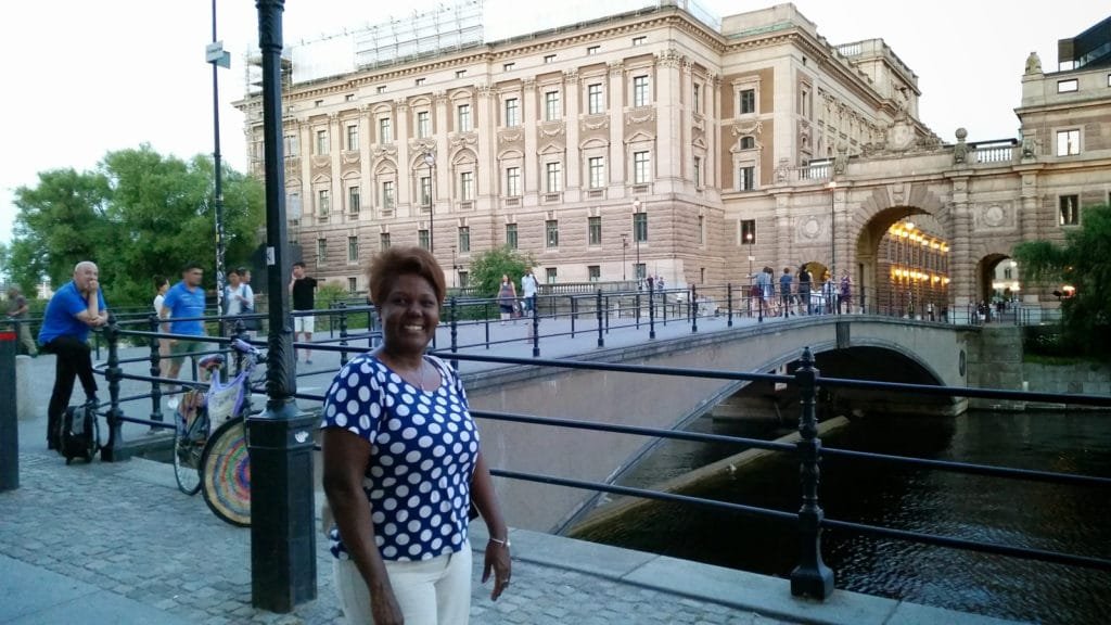 Turist som poserer ved en historisk bro med et palass i bakgrunnen i Stockholms skjærgård.