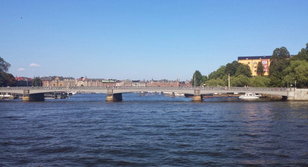 Elveutsikt med bro og bygninger under klar blå himmel i Stockholms skjærgård.