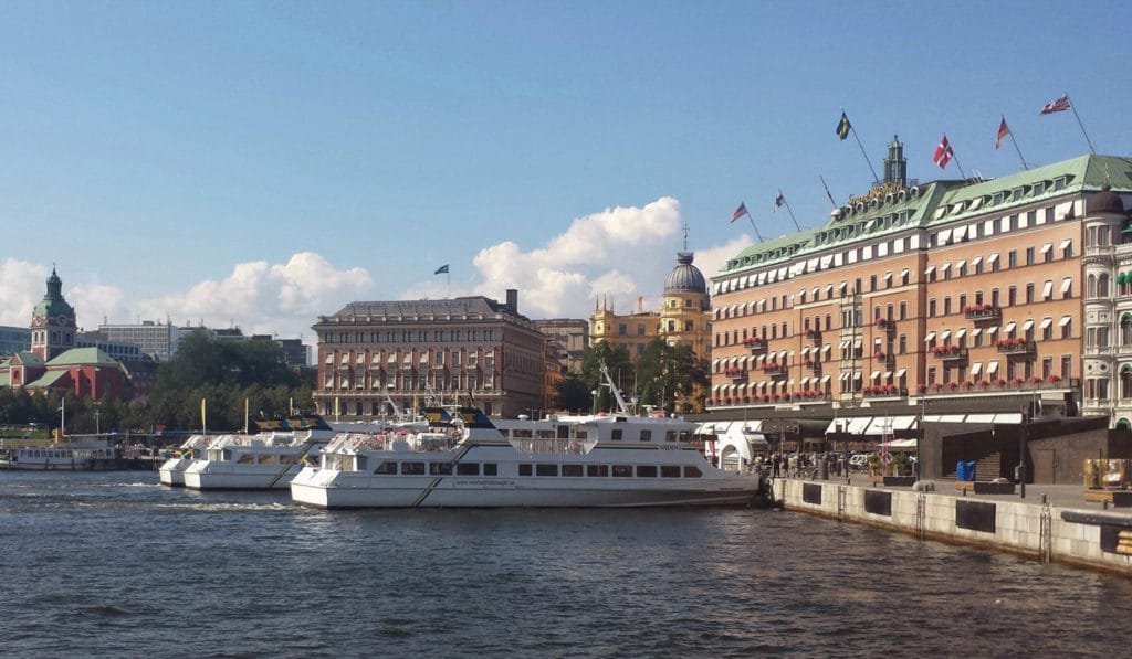 Utsikt over Stockholms skjærgård med båter i vannet og historiske bygninger under klar blå himmel på en solrik sommerdag.