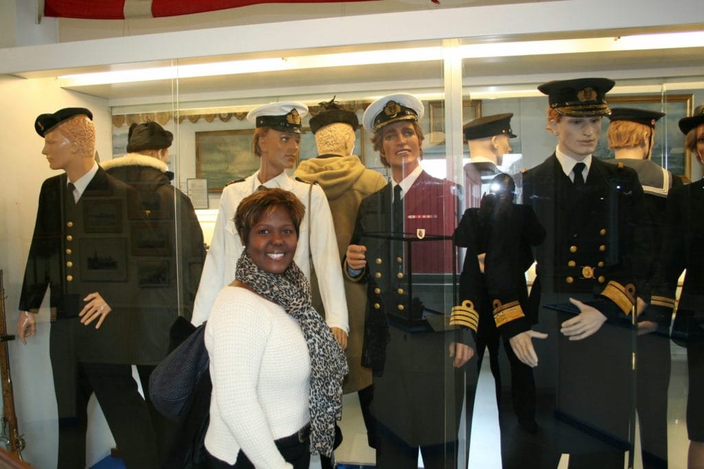 Kvinne poserer foran en utstilling med vintage pilot- og flyvertinneuniformer.