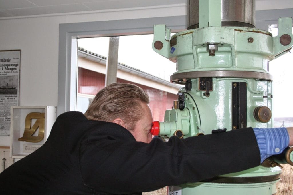 Mann som ser gjennom et gammelt optisk instrument i et museumsrom.