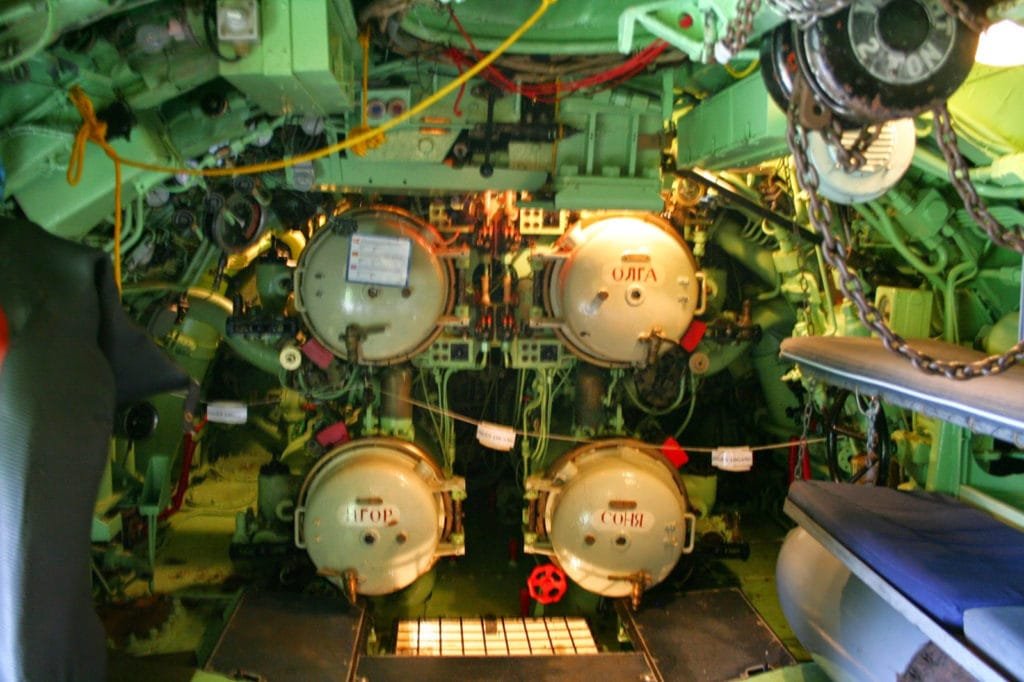 Interiør fra ubåtens torpedorom med torpedotuber og teknisk utstyr.