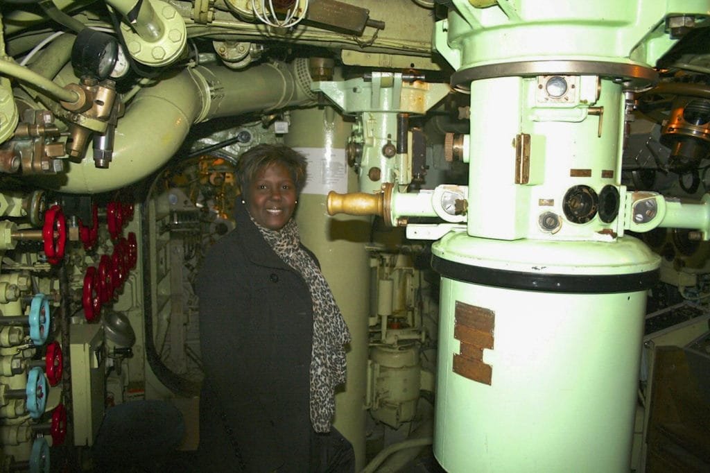 Kvinne står inne i et ubåtkontrollrom omgitt av maskineri og rør.