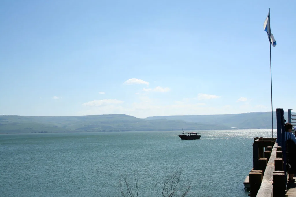 Genesaretsjøen i Israel med en turbåt på stille vann og åser i bakgrunnen under en klar blå himmel.