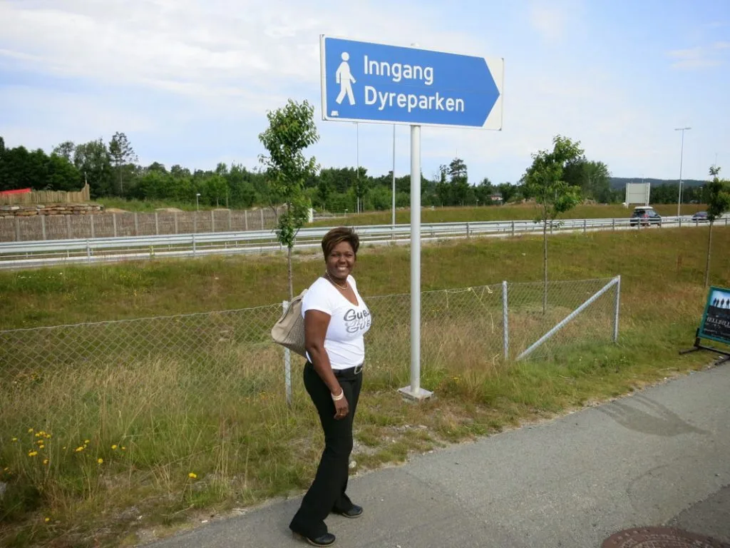 Kvinne står ved veikryss ved et skilt som peker mot inngangen til Kristiansand Dyrepark.