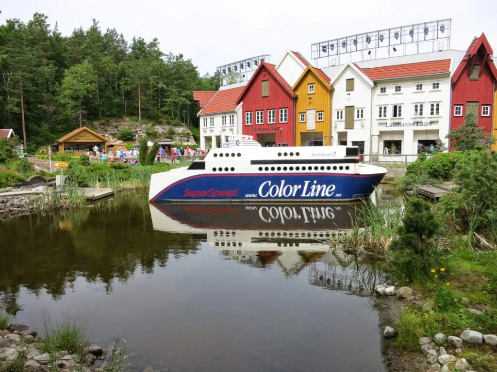 Fargerike hus ved vannkanten i en idyllisk landsby med en Color Line-ferge som speiles i det rolige vannet.