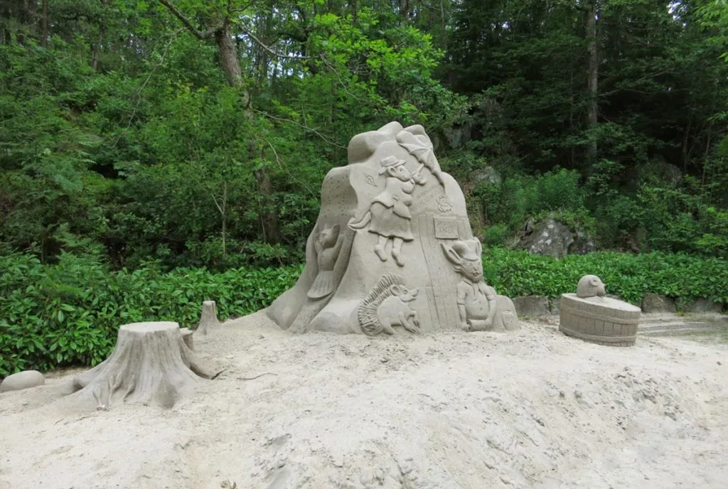 Detaljert sandskulptur av en trestubb med naturmotiv i en park.