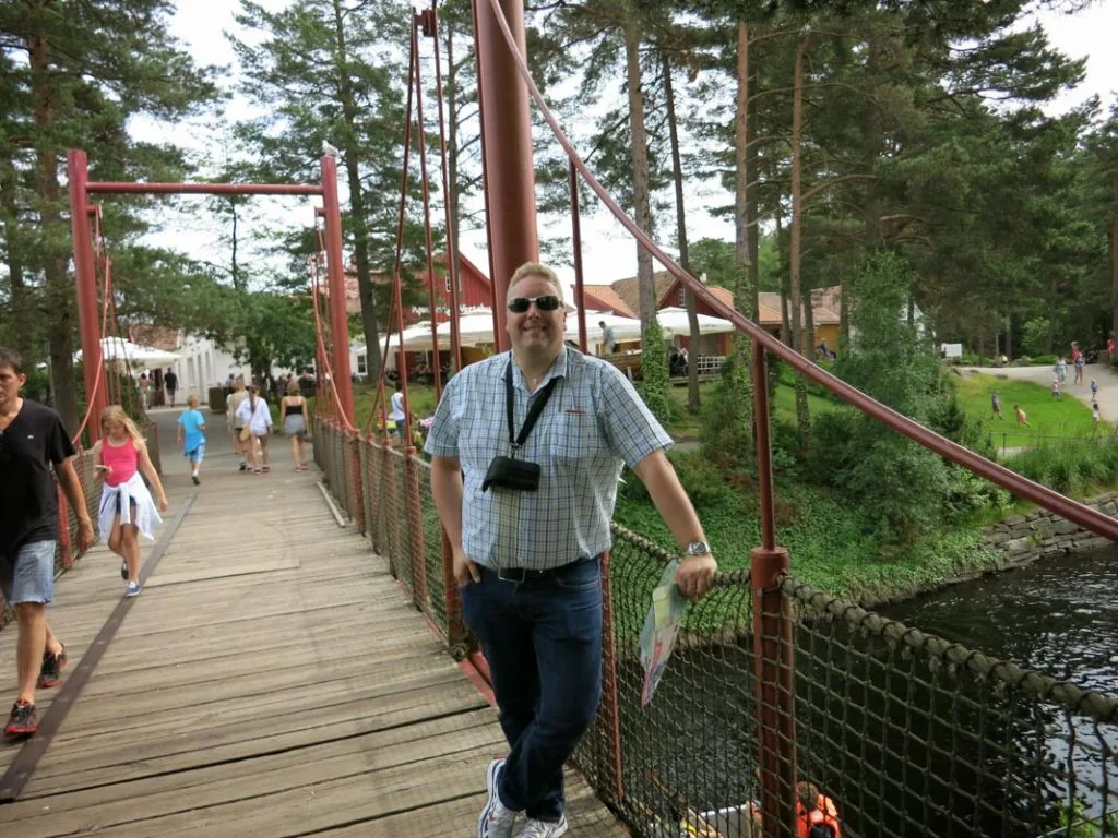 Mann som står på en hengebro i en skogkledd dyrepark.