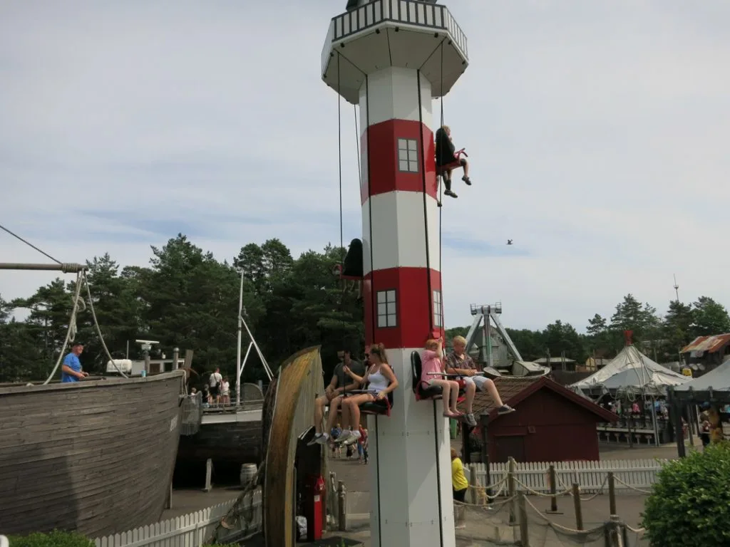 Barn som klatrer og leker på en rød og hvitstripet lekeplassstruktur formet som et fyrtårn.
