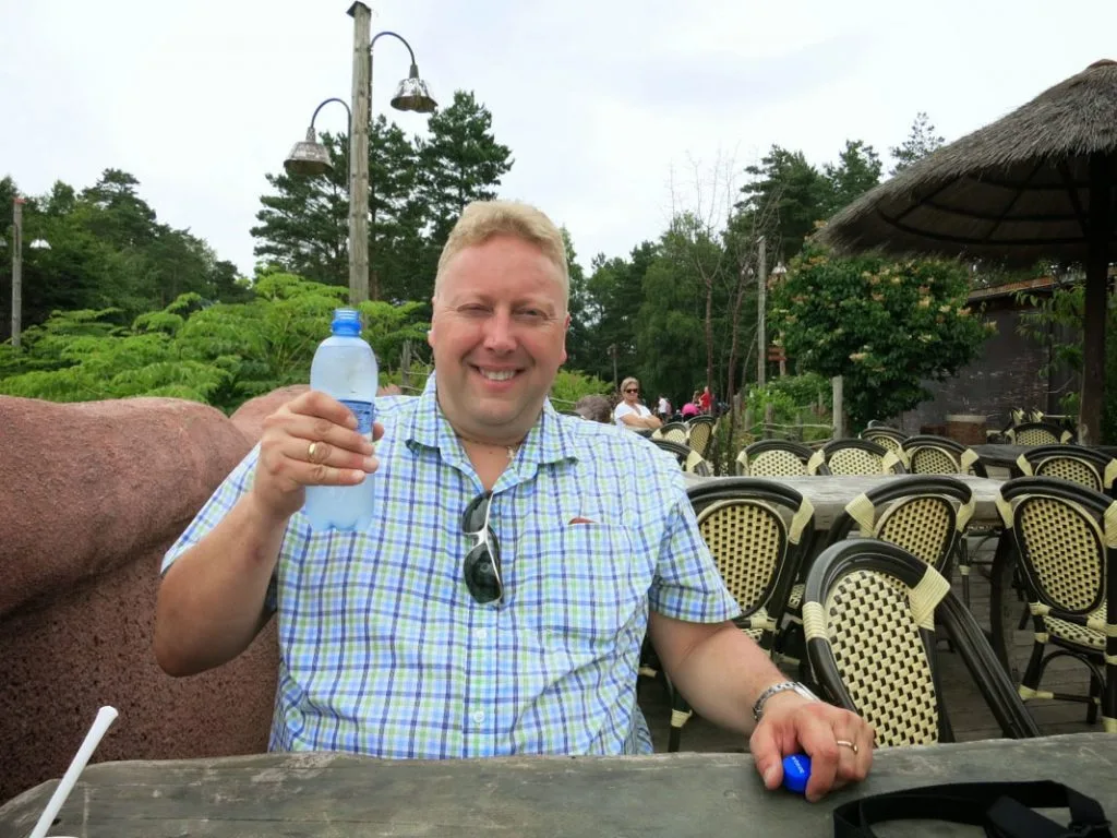 Smilende mann som sitter på en utendørs kafé og holder en vannflaske.